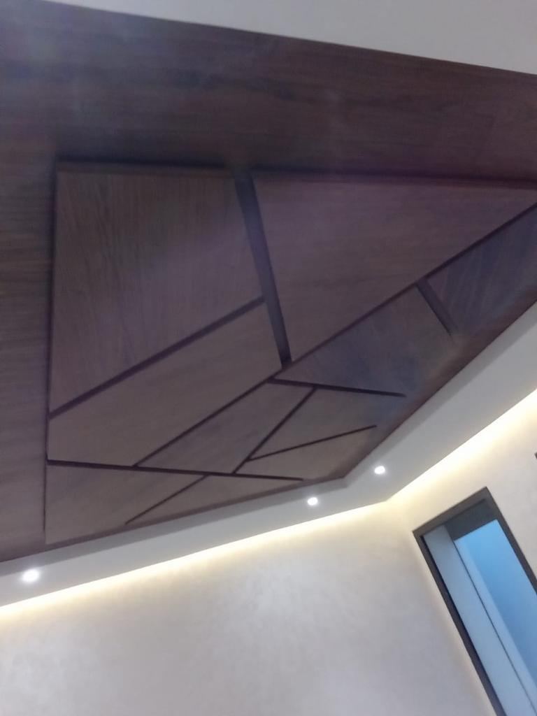 سقف مستعار من خشب داكن بنمط هندسي من خطوط منكسرة، مع إضاءة غير مباشرة على المحيط.