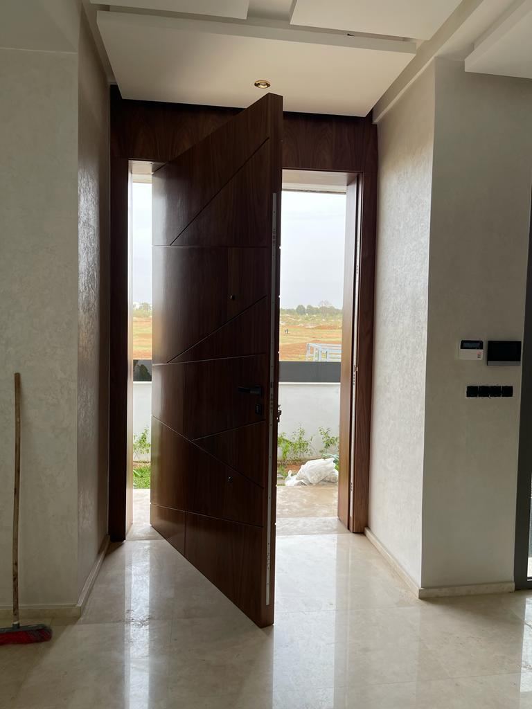 باب محوري من خشب داكن مفتوح جزئيًا على الخارج، بإطار بكامل الارتفاع وأرضية من الحجر الفاتح.